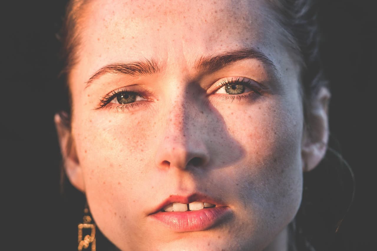 A freckled woman with natural, untouched brows, looking up