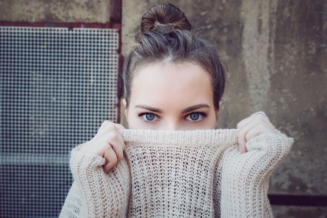 A woman with neat brows holding a knitted jumper up to her nose