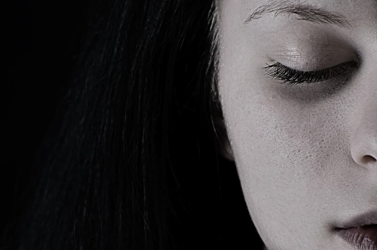 A woman in profile with her eyes closed, against black
